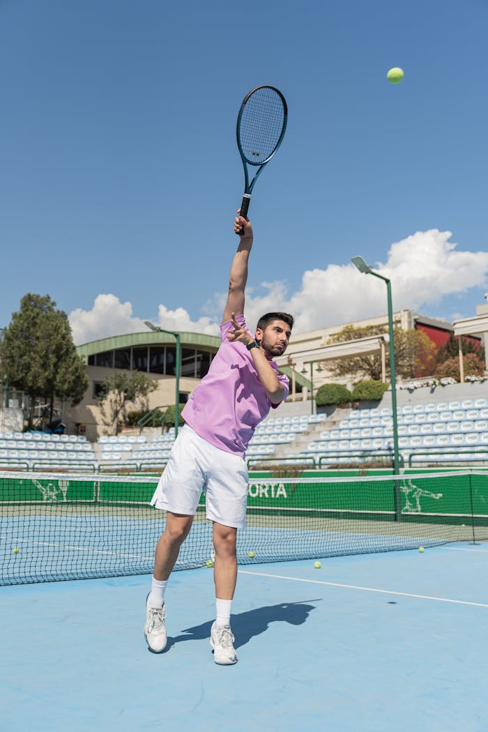 A male tennis player in action, serving on a sunny outdoor court.