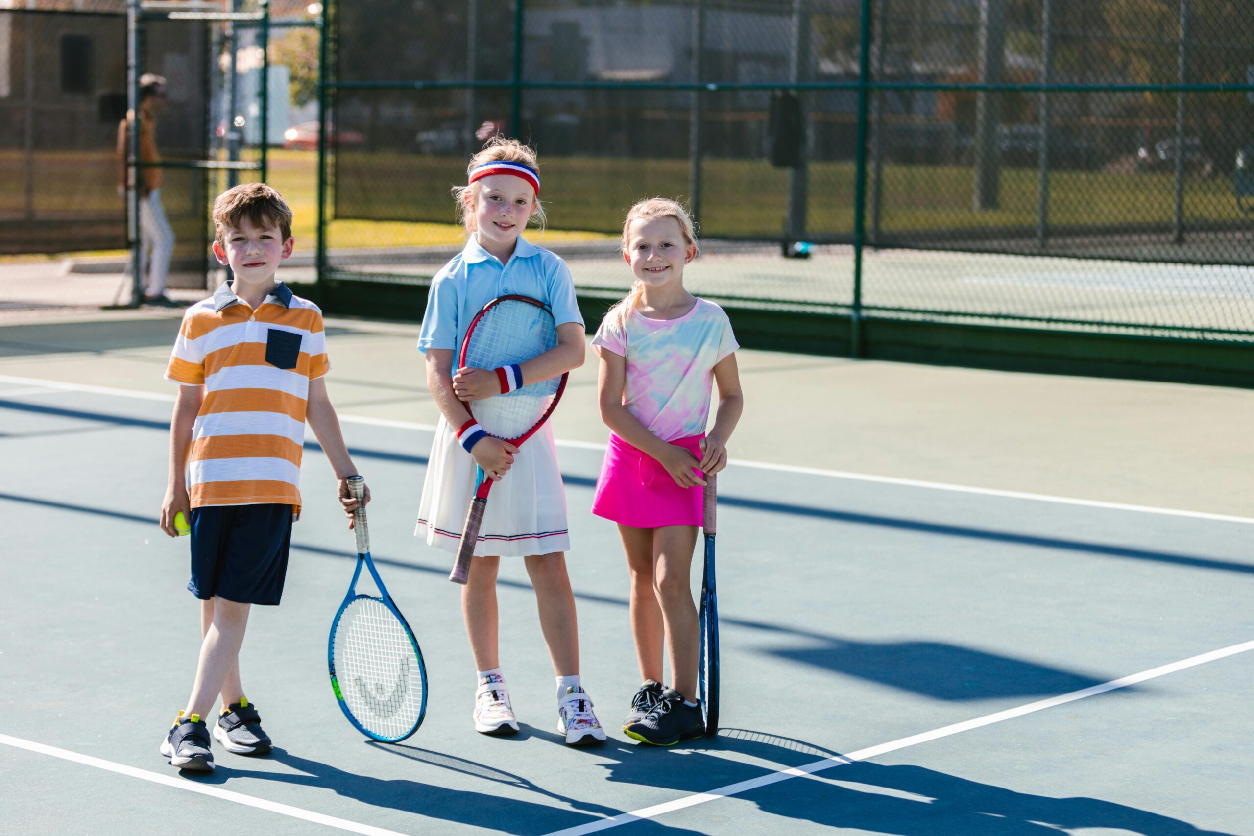 Group of kids playing tennis outdoors, showcasing teamwork and joy on a bright sunny day.
